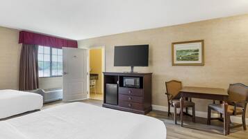 A hotel room with a bed, a TV, a microwave, a dining table with chairs, and a painting on the wall.