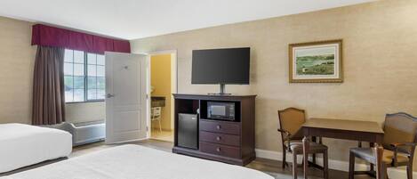 A hotel room with a bed, a TV, a microwave, a dining table with chairs, and a painting on the wall.