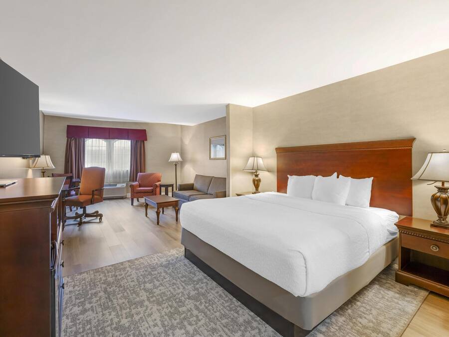 A hotel room with a large bed, a desk, a chair, a sofa, and a TV.