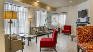 A spacious living room with a sofa, red armchair, and a television mounted on the wall. - Best Western Plus Vineyard Inn & Suites (Penn Yan)