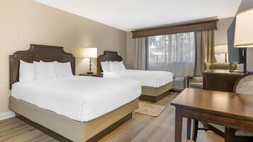 Una habitación de hotel con dos camas, un escritorio de madera, una silla y una ventana con cortinas.