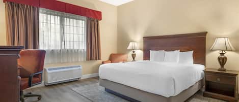 A hotel room with a large bed, two bedside lamps, a desk with a chair, and a window with curtains.