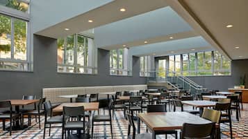A spacious indoor dining area with multiple tables and chairs, large windows, and a staircase leading to an upper level.