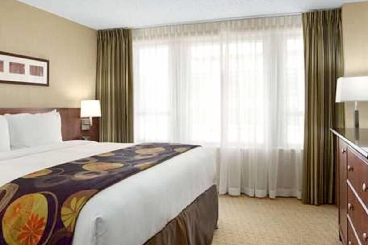 A hotel room with a bed, a nightstand, a dresser, and a window with curtains.