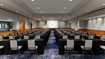 A conference room with rows of tables and chairs, a large screen, and a carpeted floor.