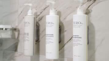Tres botellas de champú y acondicionador 'ZERO%' sobre una pared con azulejos de mármol.