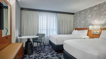 A hotel room with two beds, a small table with a chair, a bench, a TV, and a large window with curtains.
