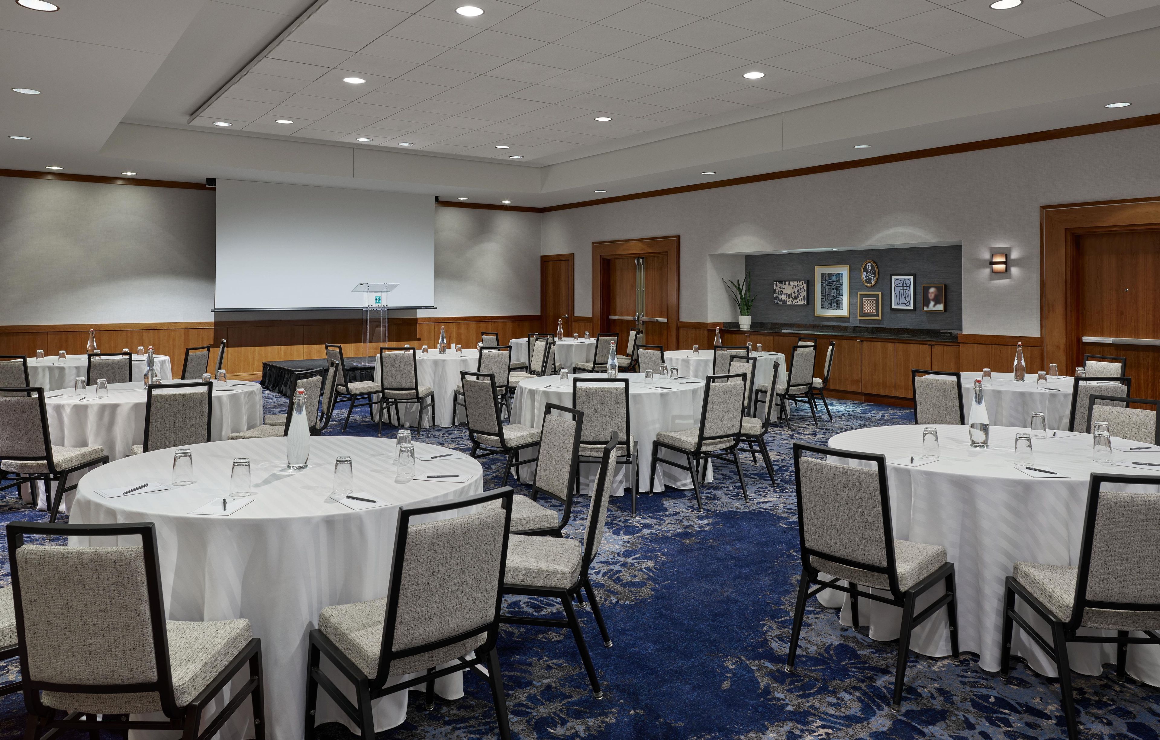A conference room with round tables, chairs, and a projector screen.