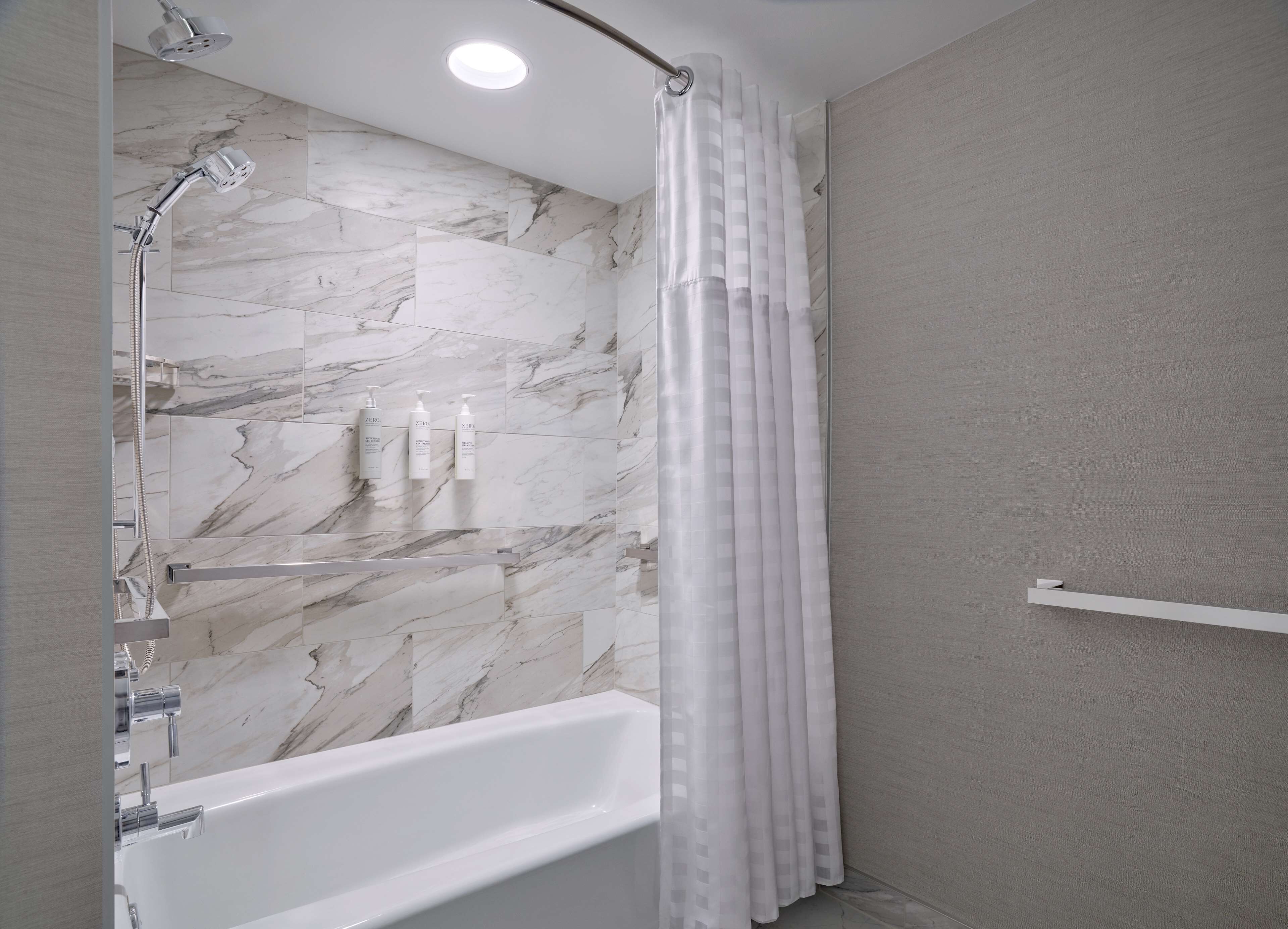 A modern bathroom with a marble shower wall, a white bathtub, and a shower curtain.