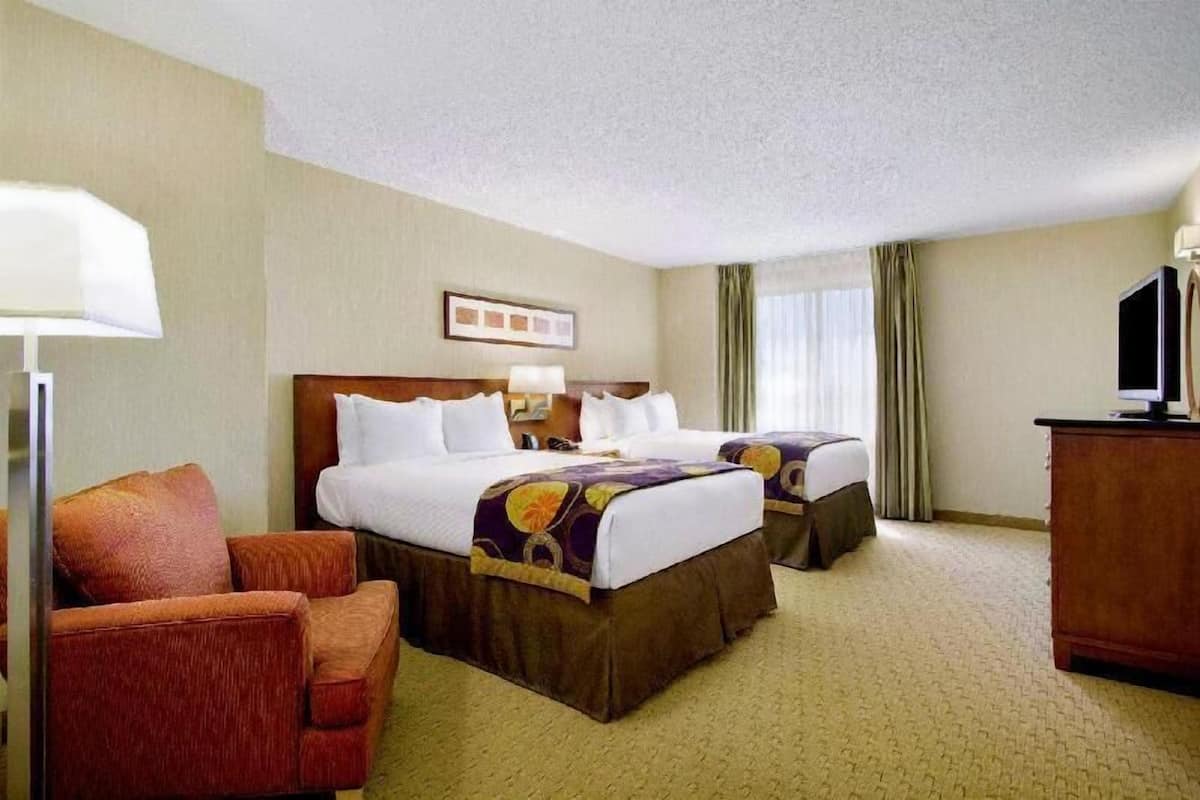 A hotel room with two beds, a desk, a chair, and a television.