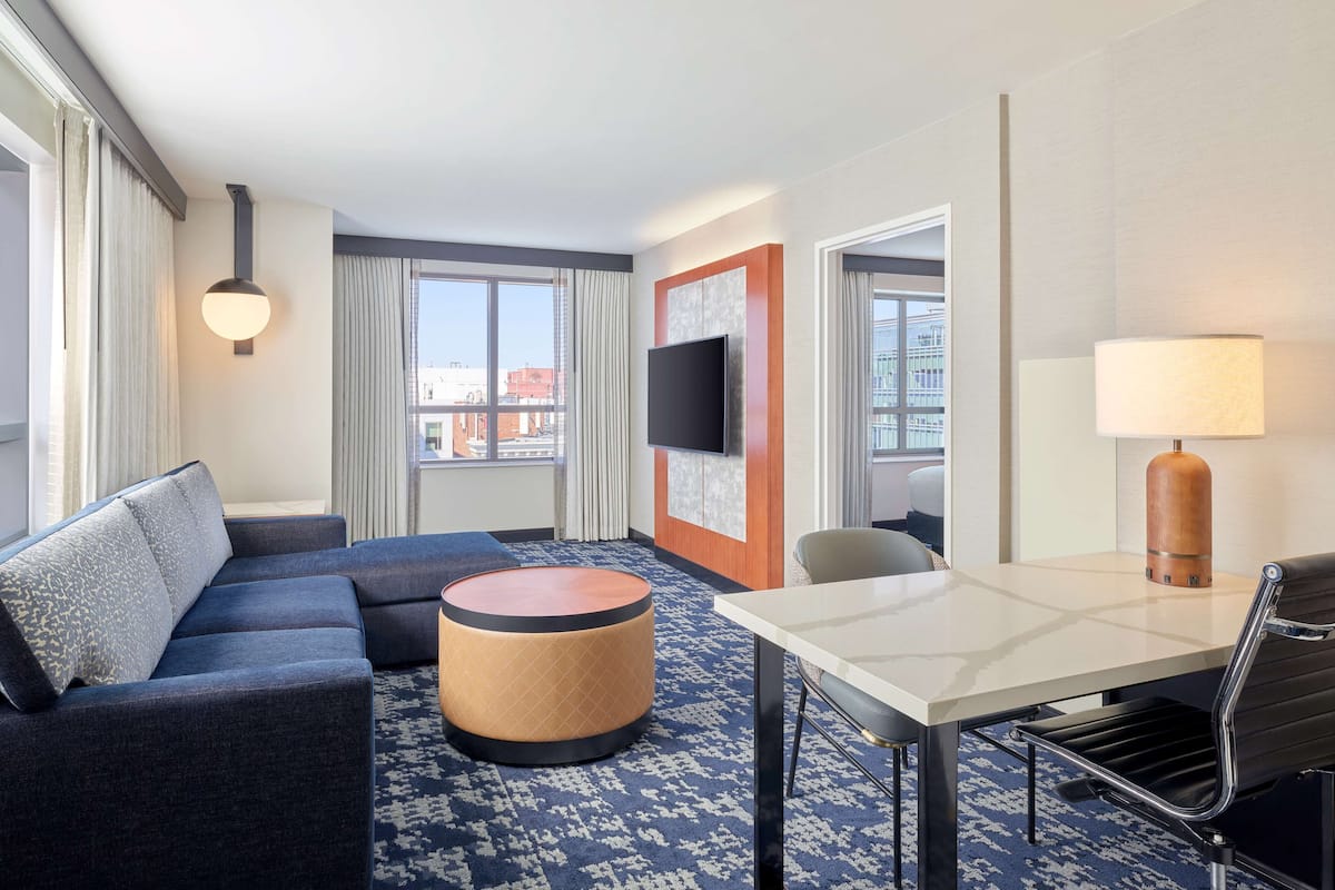 A hotel room with a sofa, ottoman, dining table, and chairs.