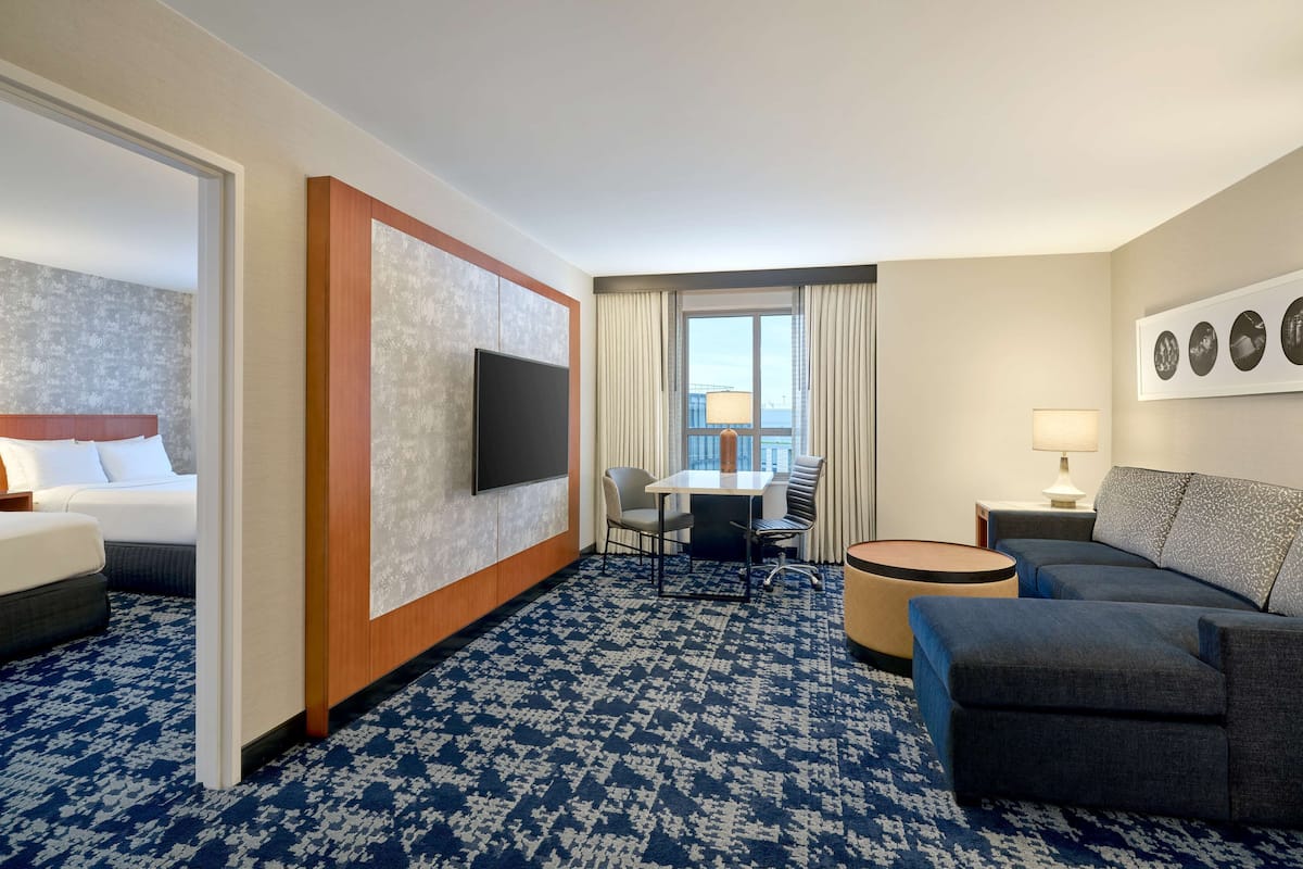A hotel room with a bed, a TV, a dining table with chairs, a sofa, and a small round table with a lamp.
