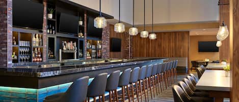 A bar area with a long counter, multiple seating options, and a television mounted on the wall.