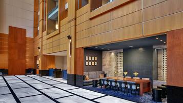 A spacious lobby with a marble floor, a reception desk, a seating area with a sofa and chairs, and a dining area with a table and chairs.