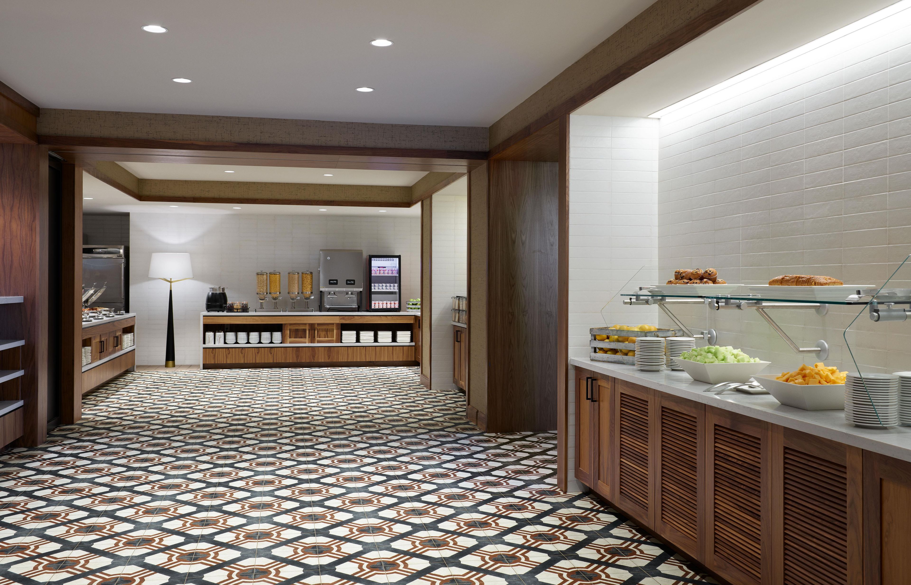 A modern kitchen with a patterned floor, wooden cabinets, and a buffet area with various food items.