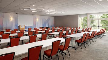 Une salle de conférence avec des rangées de tables et de chaises, un écran de projection et un pupitre pour les présentations.