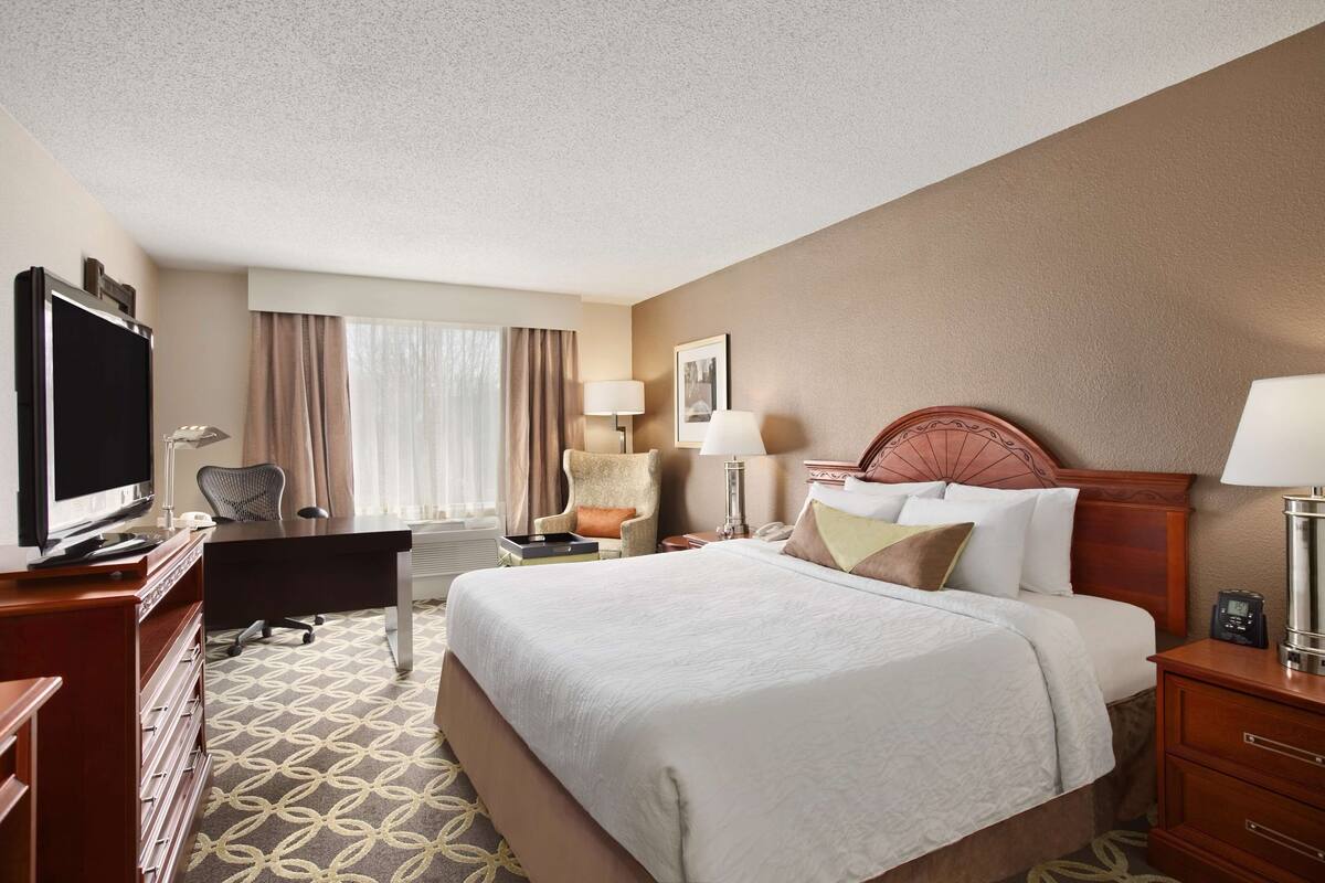 A hotel room with a bed, desk, television, and a window with curtains.
