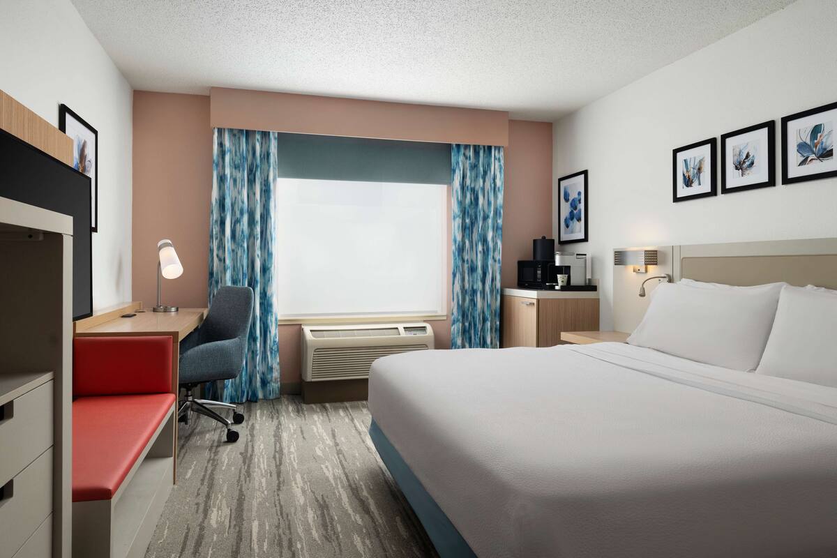 A hotel room with a bed, desk, chair, and a window with curtains.