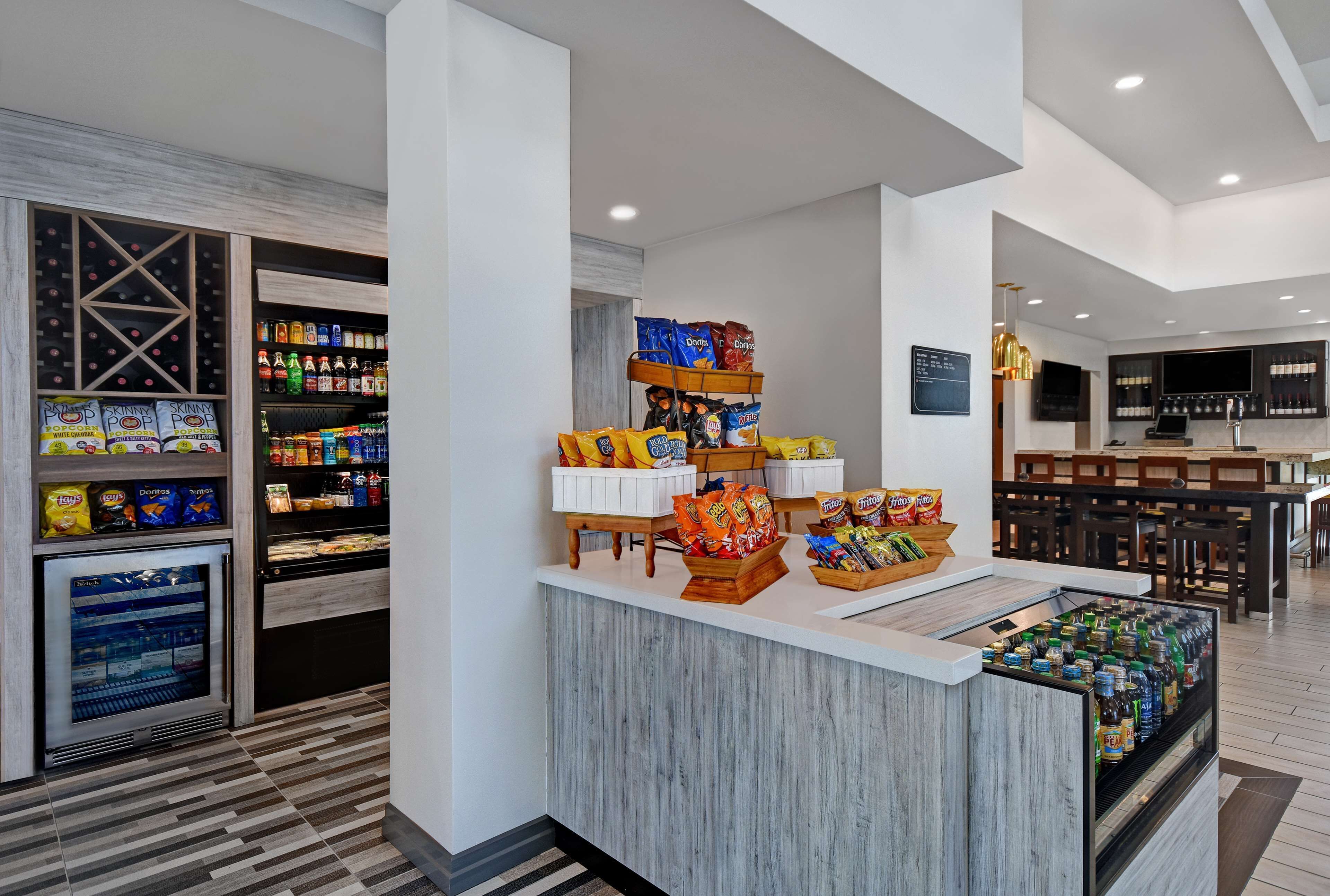 Un moderno vestíbulo de hotel con un bar de aperitivos, dispensadores de bebidas y una zona de estar.