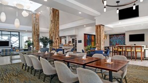 A modern hotel lobby with a large dining area, comfortable seating, and a large TV screen. - Hilton Garden Inn Houston/Galleria Area (Houston)