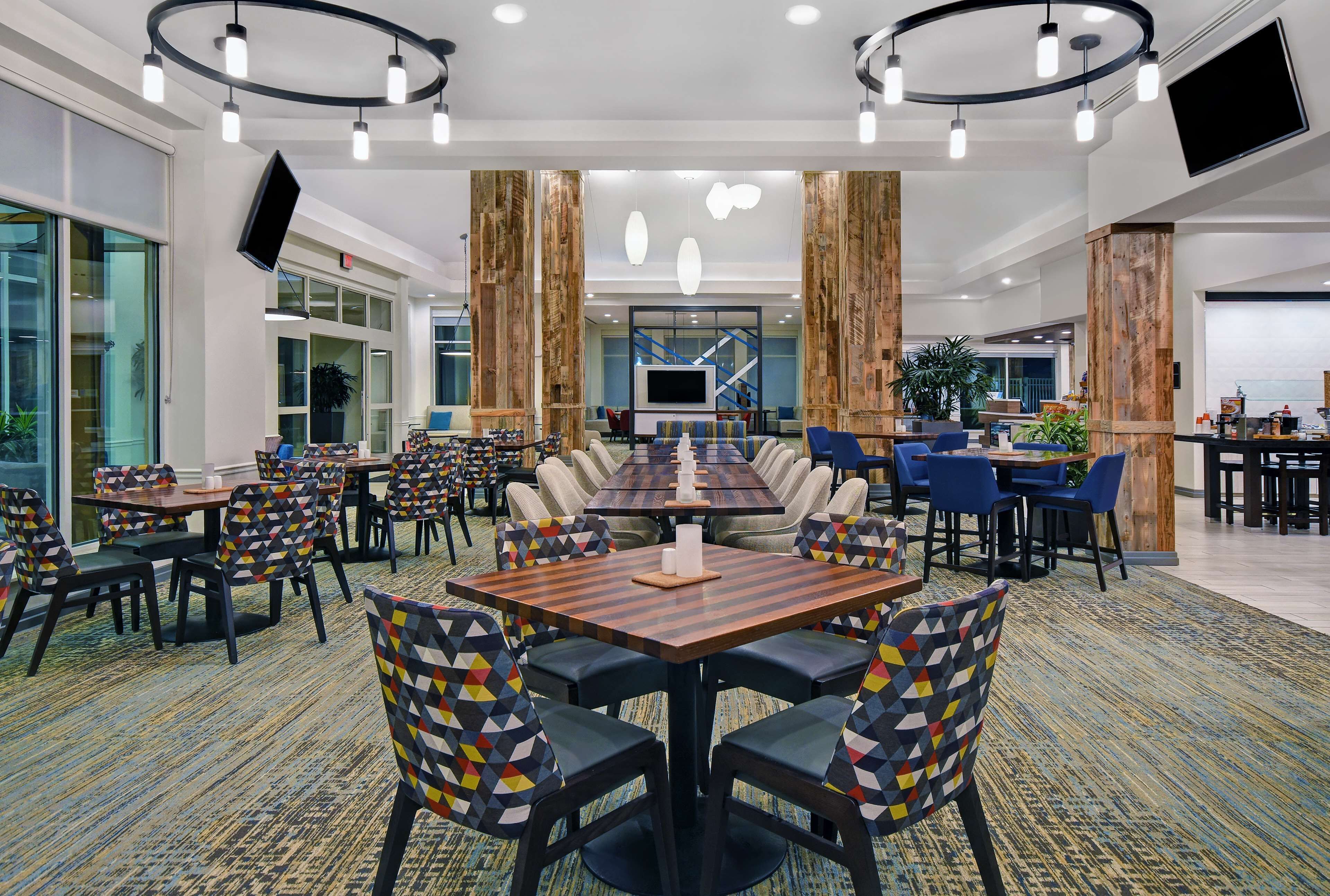 A spacious dining area with a long table and multiple chairs, surrounded by wooden pillars and modern lighting fixtures.