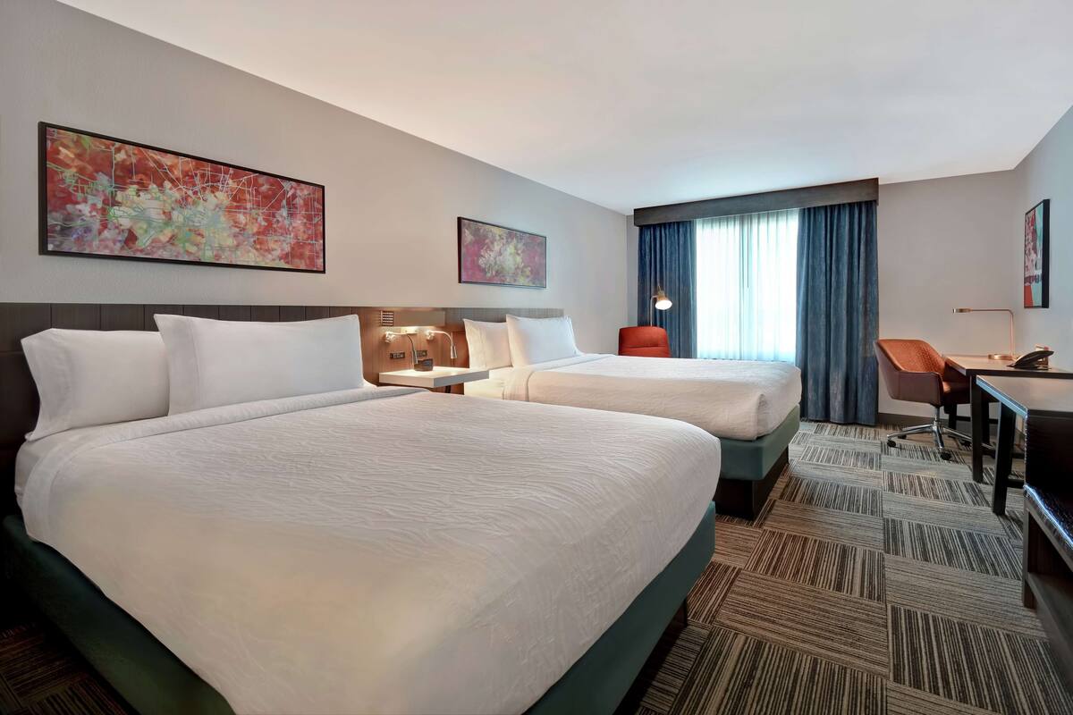 A hotel room with two beds, a desk, a chair, and artwork on the walls.