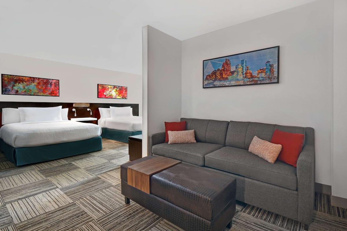 A hotel room with a bed, a sofa, a coffee table, and two paintings on the wall.