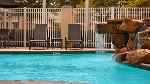 A swimming pool with a waterfall feature, surrounded by a white fence and two wicker chairs. - Hilton Garden Inn Houston/Galleria Area (Houston)
