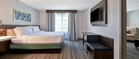 A hotel room with a bed, a desk, a TV, and a window with curtains.