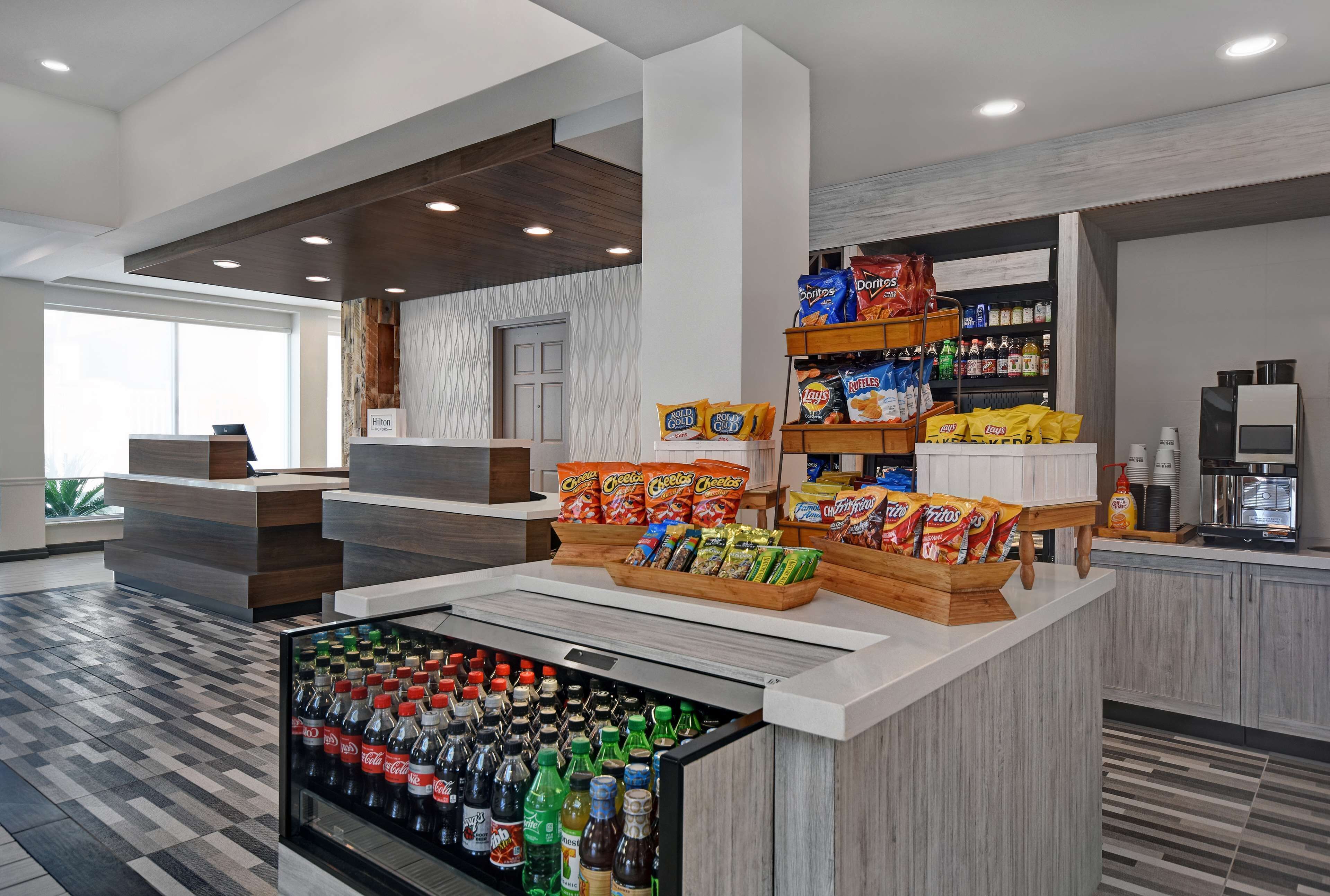 A hotel lobby with a reception desk, a beverage cooler, snack shelves, and a coffee station.