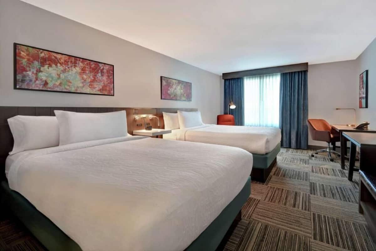 A hotel room with two beds, a desk, a chair, and artwork on the walls.