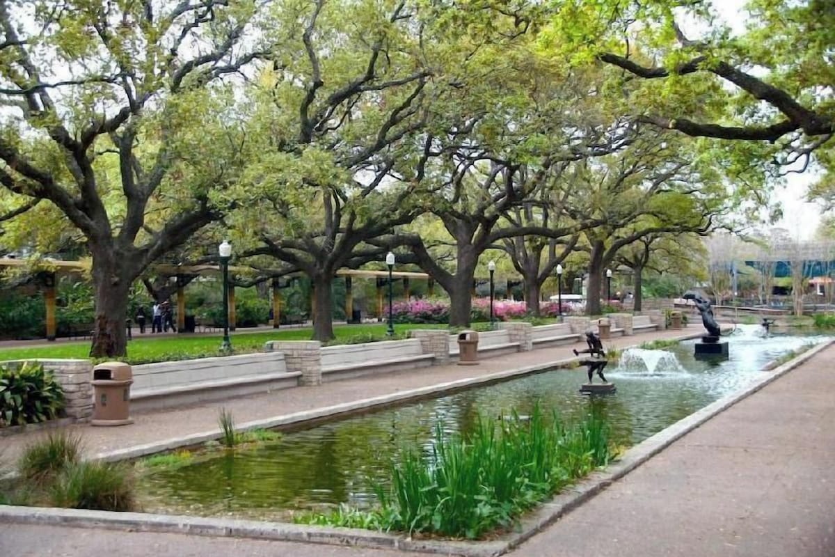 Ein Park mit einem Wasserspiel, Bäumen und einem Weg.