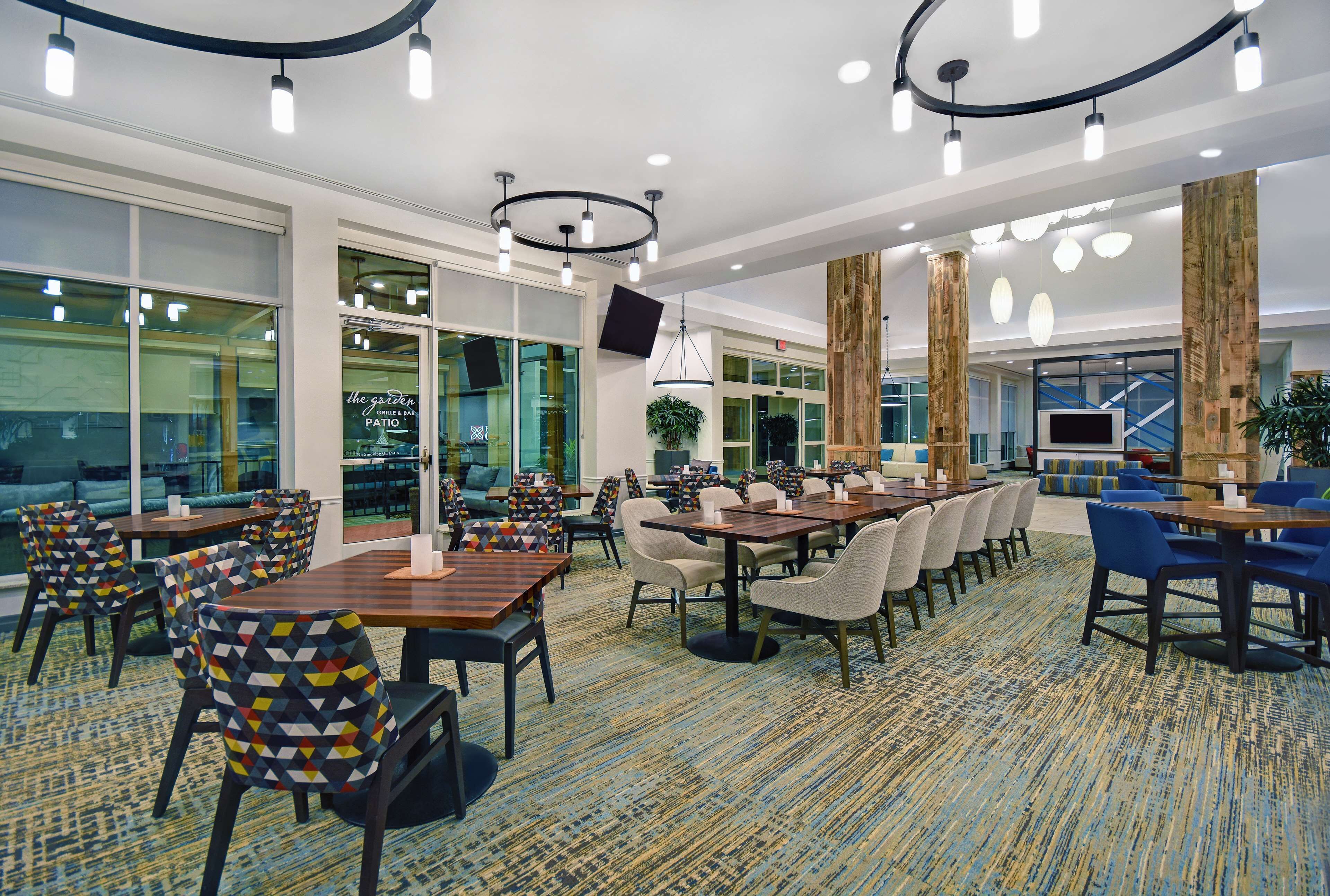 A modern hotel lobby with multiple seating areas, large windows, and a variety of lighting fixtures.