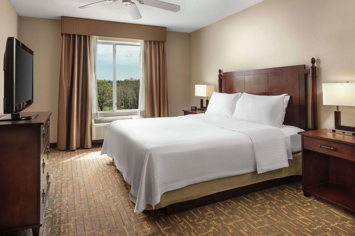 Habitación de hotel con cama, televisión, escritorio y ventana con cortinas.
