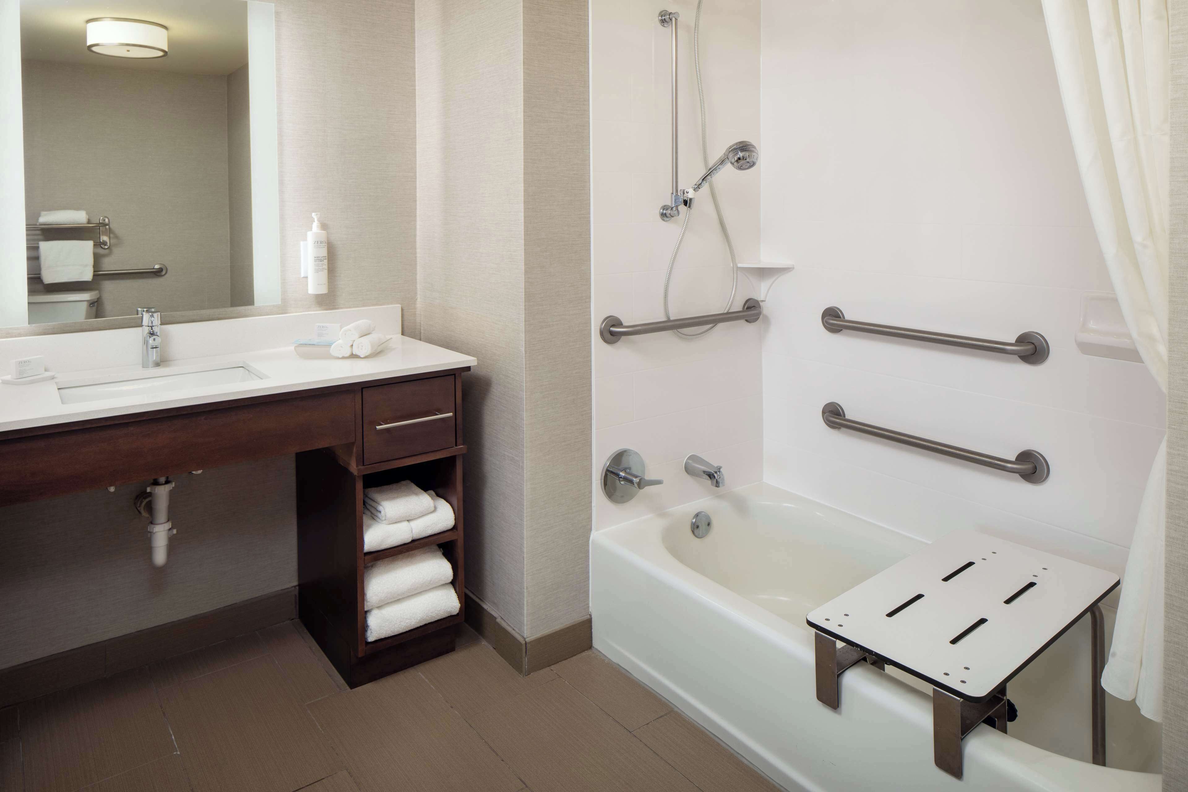 A modern bathroom with a bathtub, a vanity with a mirror, and a shelf with towels.