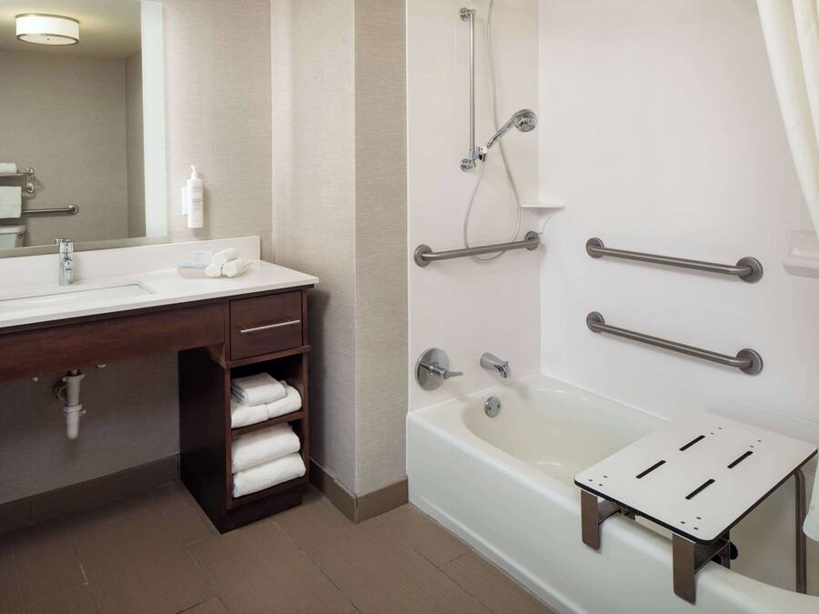 A modern bathroom with a bathtub, a vanity with a mirror, and a shelf with towels.
