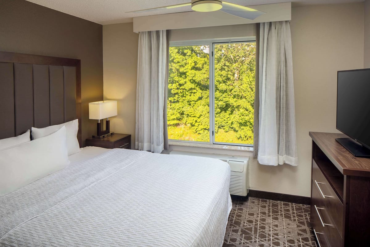 Een hotelkamer met een groot bed, een nachtkastje met een lamp, een televisie en een raam met gordijnen.