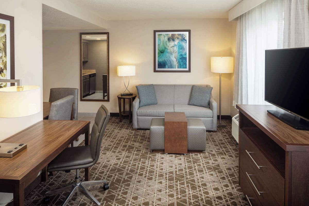 Een hotelkamer met een houten bureau, een grijze bank, een televisie en een schilderij aan de muur.