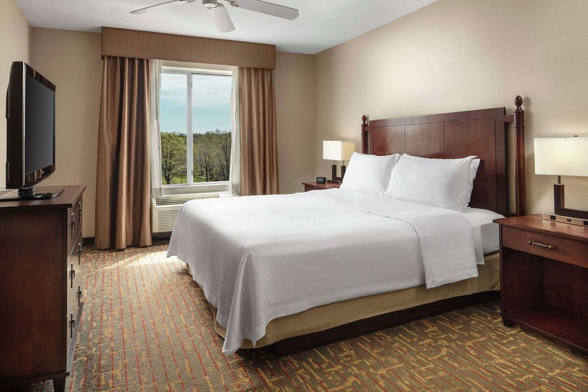 Habitación de hotel con cama, televisión, escritorio y ventana con cortinas.