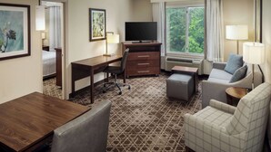 Een hotelkamer met een bed, een bureau, een televisie, een bank en een raam met uitzicht op bomen.