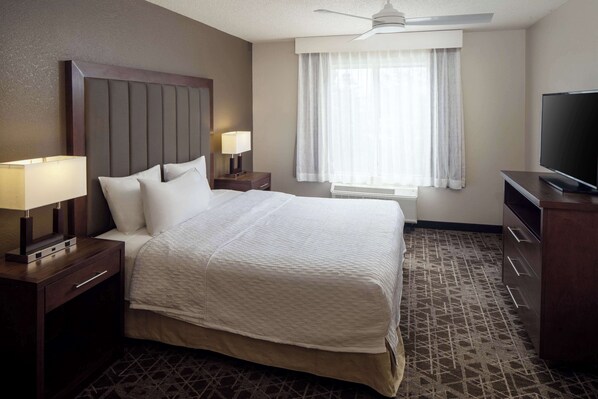 Una habitación de hotel con una cama grande, dos mesitas de noche con lámparas, un televisor y un ventilador de techo.