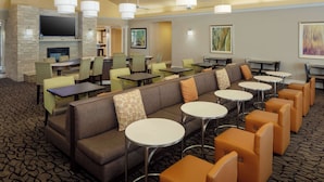 Een hotel lobby met een stenen openhaard, meerdere zithoeken, waaronder een bank en fauteuils, en een televisie die aan de muur is bevestigd.