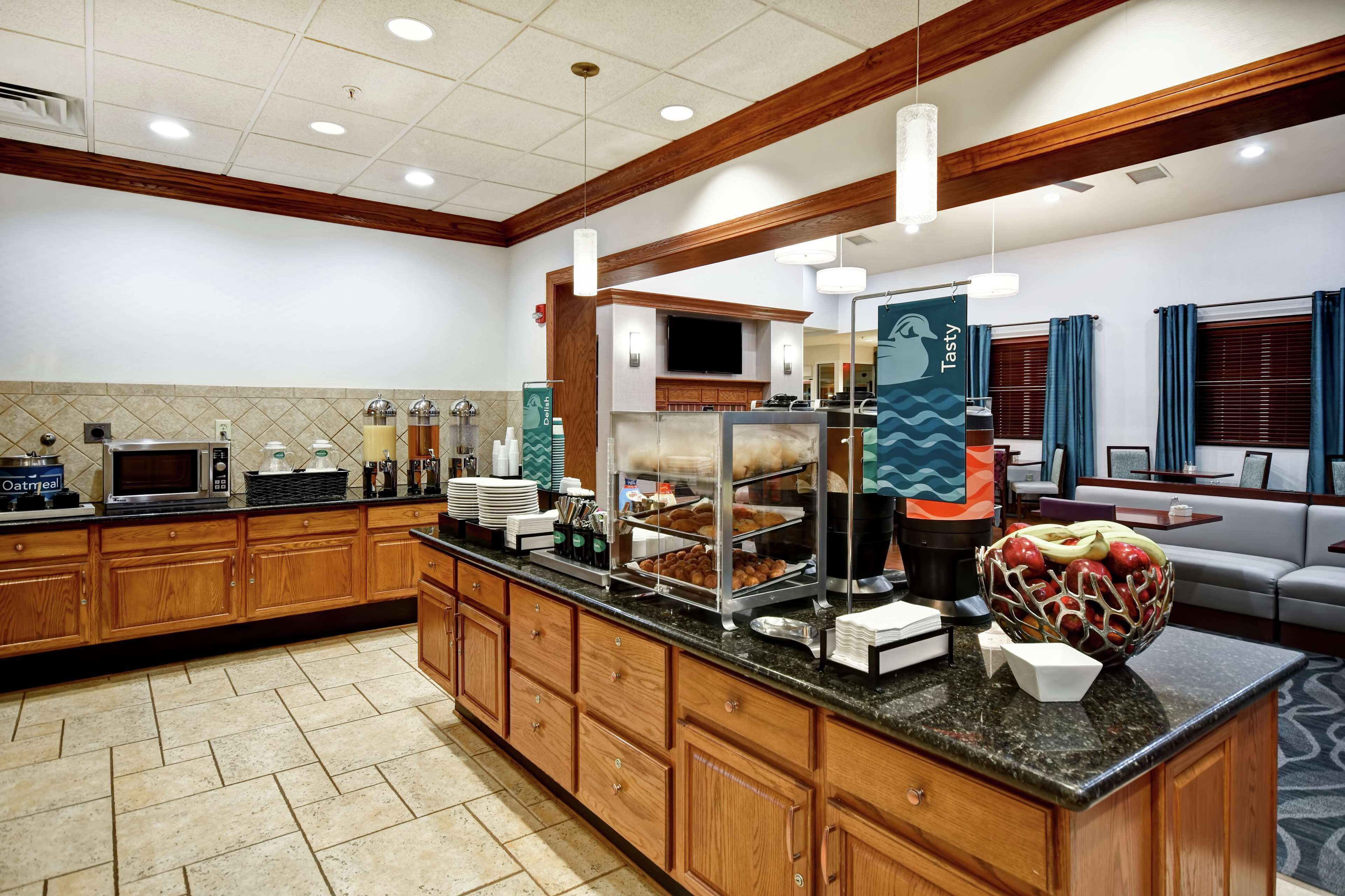 A hotel breakfast area with wooden cabinets, a buffet counter, and a seating area with a sofa and a coffee table.