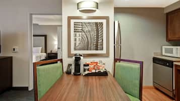 Habitación de hotel con una mesa de comedor, sillas, cafetera, aperitivos, microondas y lavavajillas.