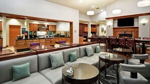 Un hall d’hôtel moderne avec un espace salon, un bar et une cuisine visible au fond.