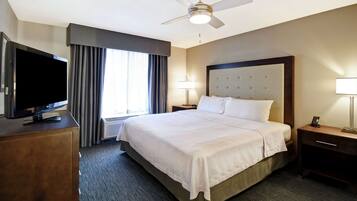 A hotel room with a large bed, a flat-screen TV, a ceiling fan, and a window with curtains.