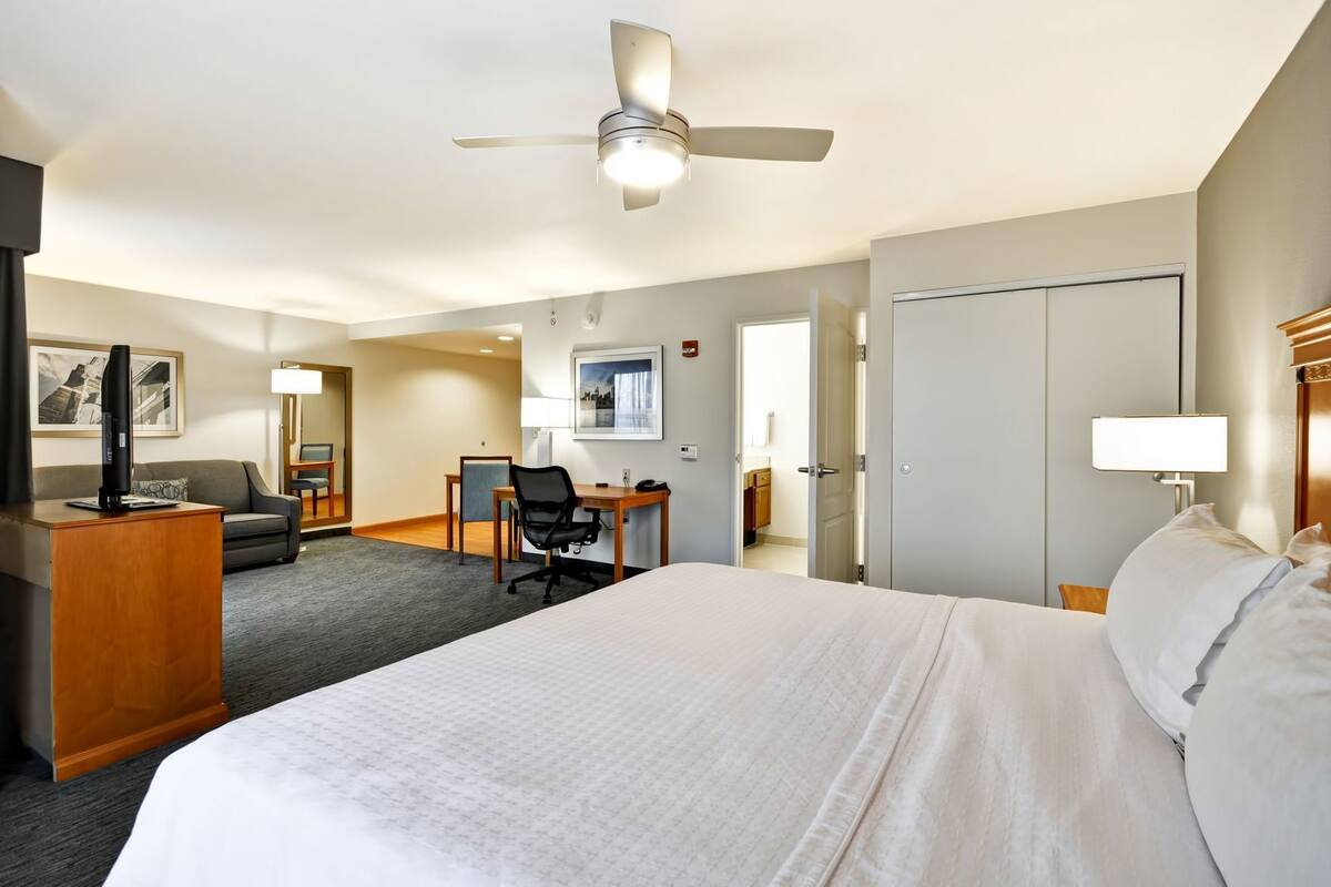 Una habitación de hotel con cama, escritorio, silla, televisor y ventilador de techo.