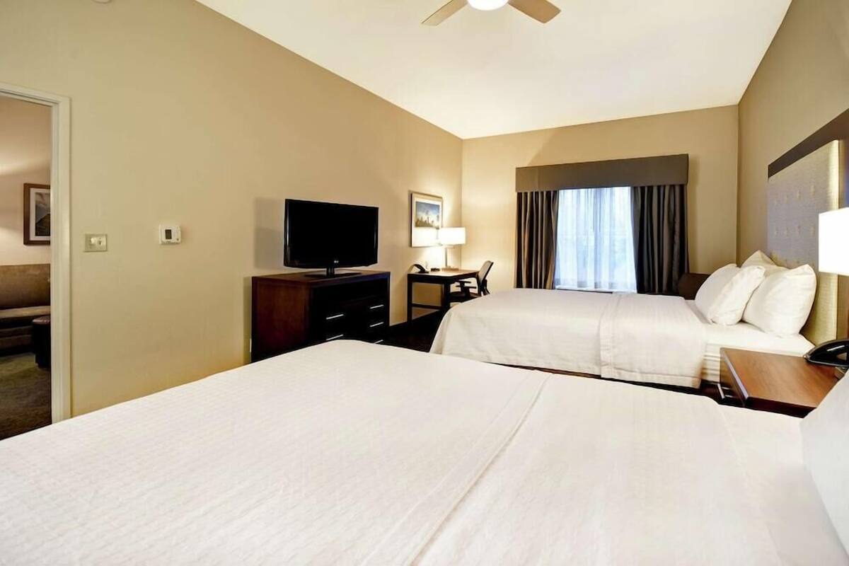 Habitación de hotel con dos camas, televisión, escritorio con lámpara y ventana con cortinas.