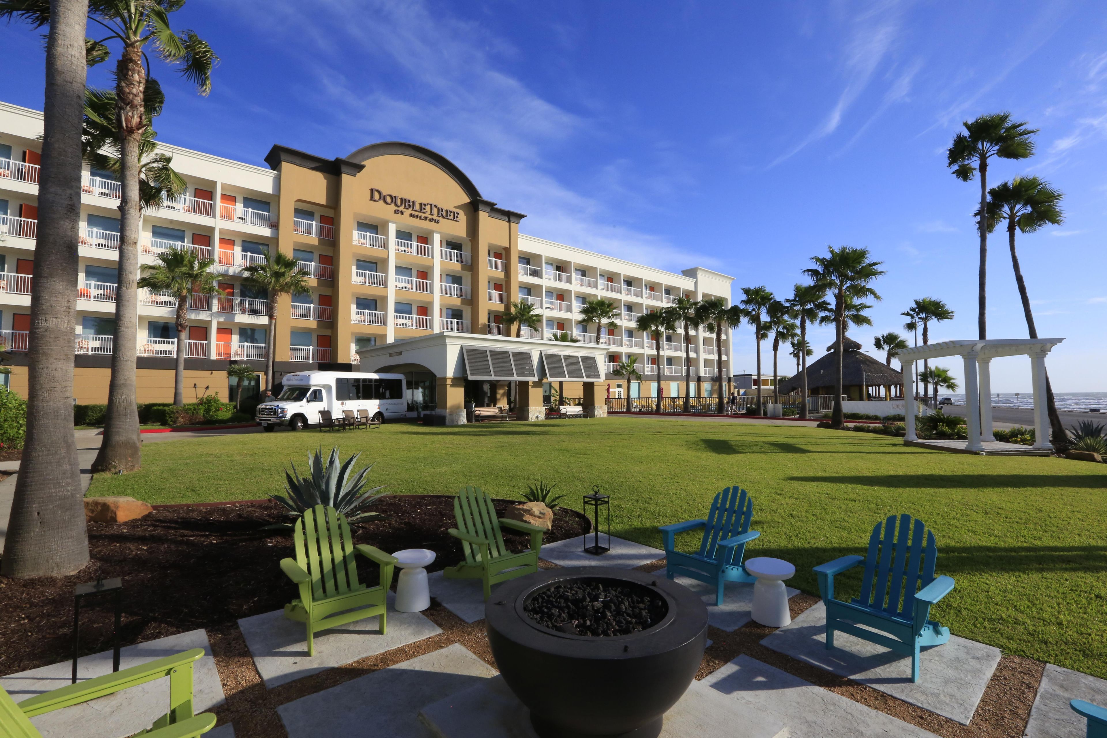 A hotel with a pool area, outdoor seating, and palm trees.