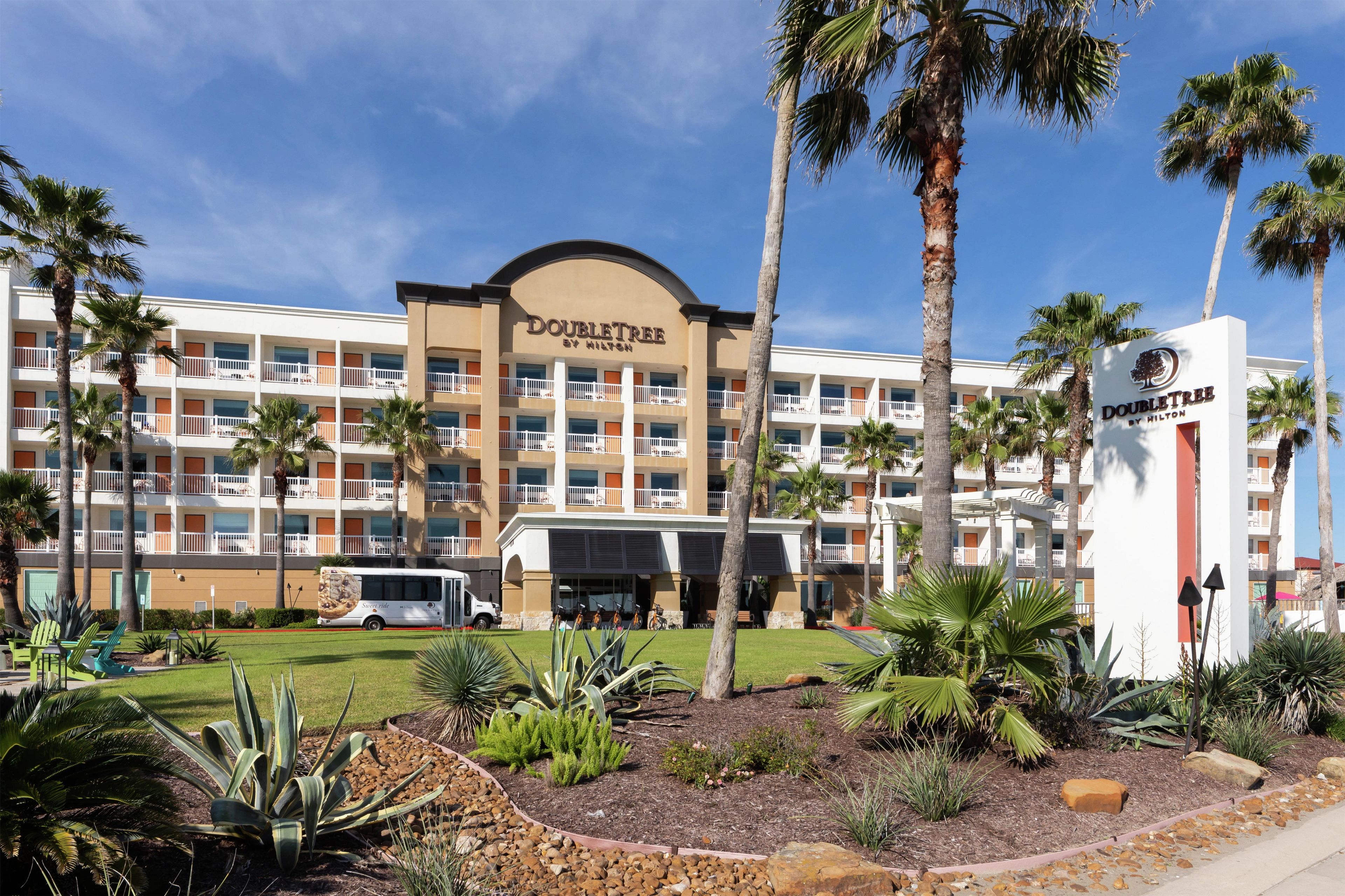 A hotel with a central entrance, multiple balconies, and palm trees.